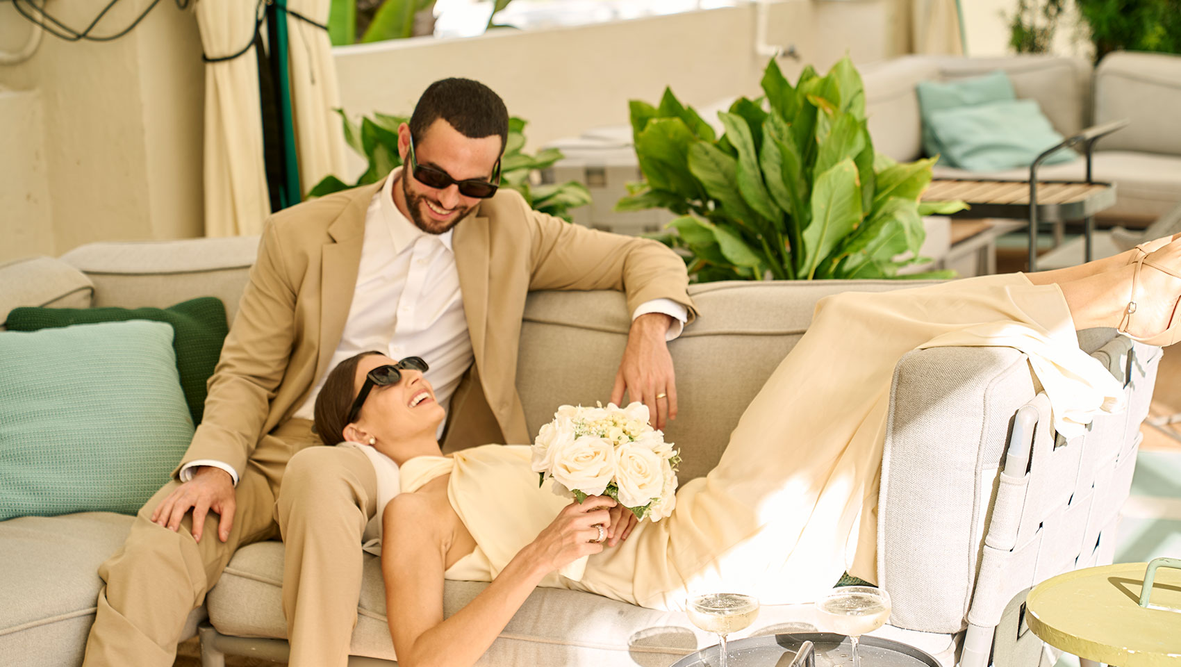Bride and groom lounge on sofa with bouquet of flowers